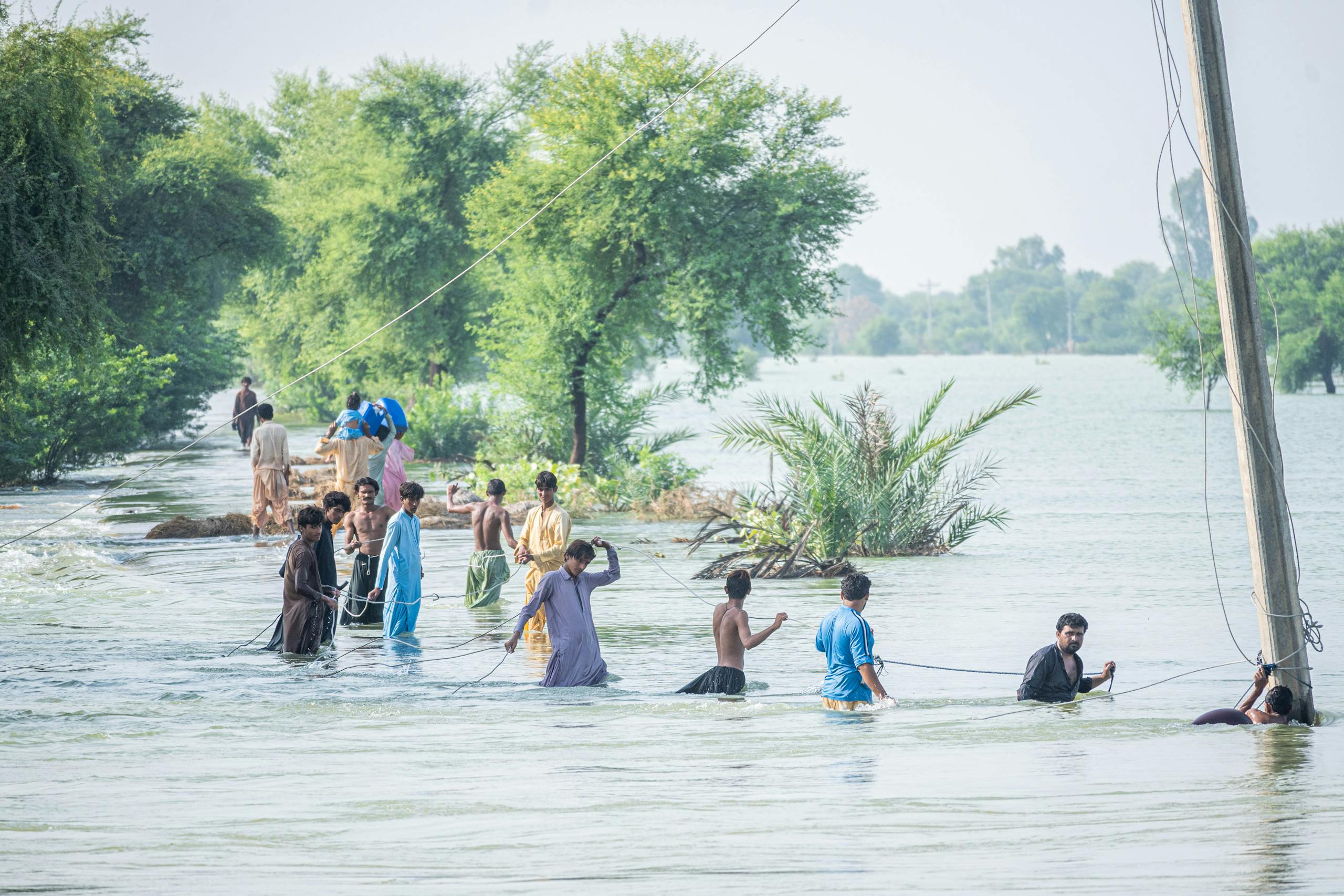 A group of people wading through a flooded area in Manjhoo Shori, Balochistan, showcasing resilience.
